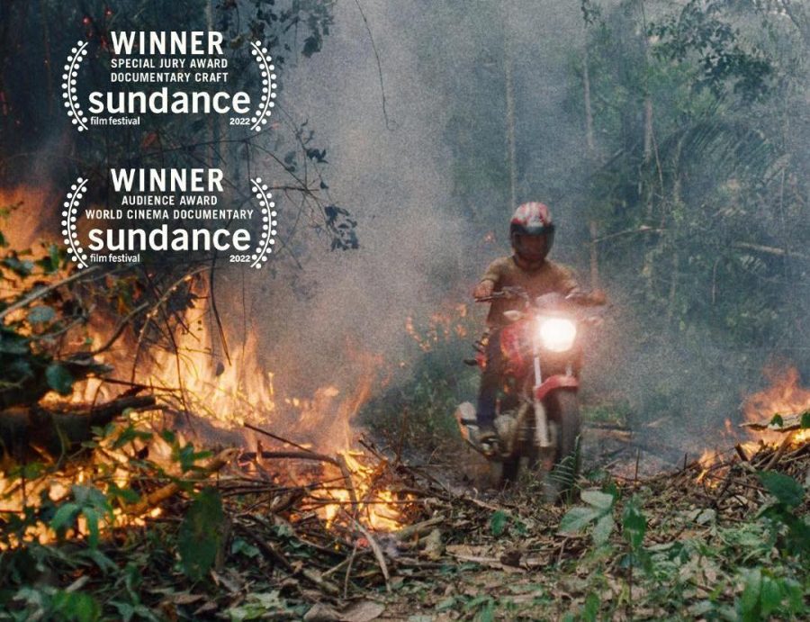 A settler drives a motorcycle through a burning section of rainforest. 